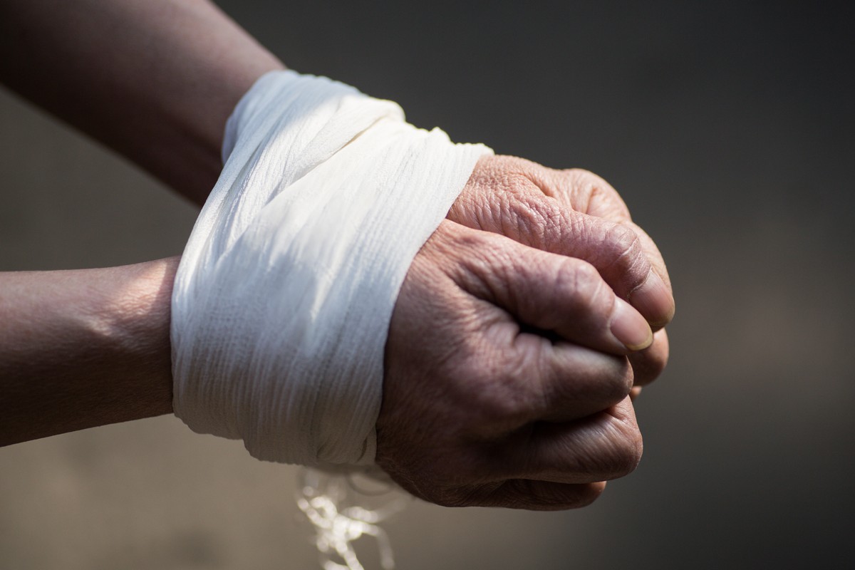 A closeup of tied hands of a middle-aged woman on a blurred gray background